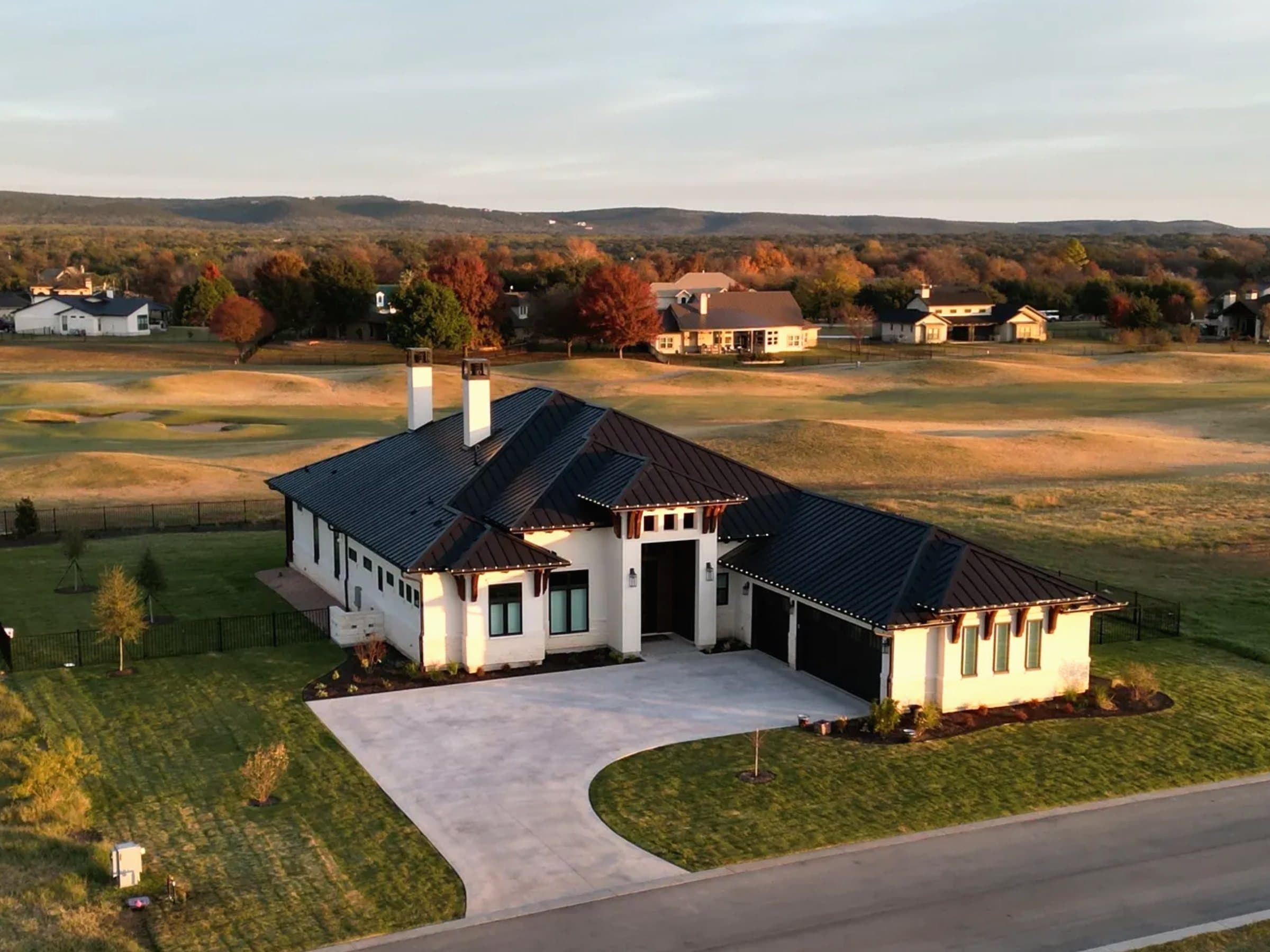 Aerial view of a finished home at golden hour, Hill Country trees turning beyond