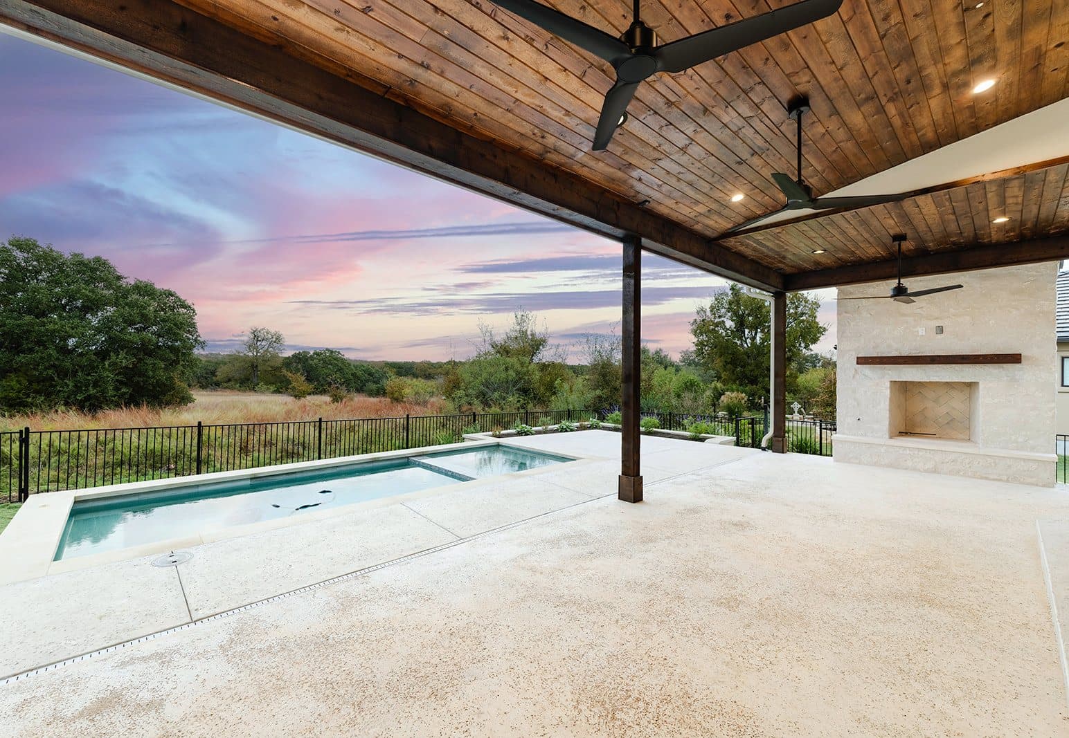 Covered patio with a stained tongue-and-groove ceiling and stone fireplace, the pool beyond at dusk