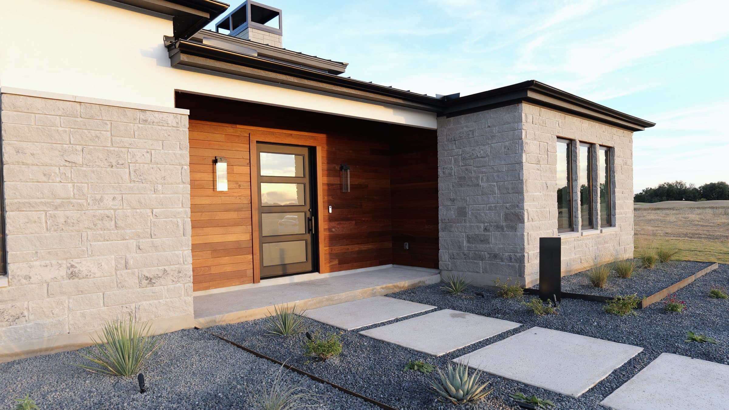 Recessed entry clad in stained wood between cut-limestone walls, a gravel garden in front