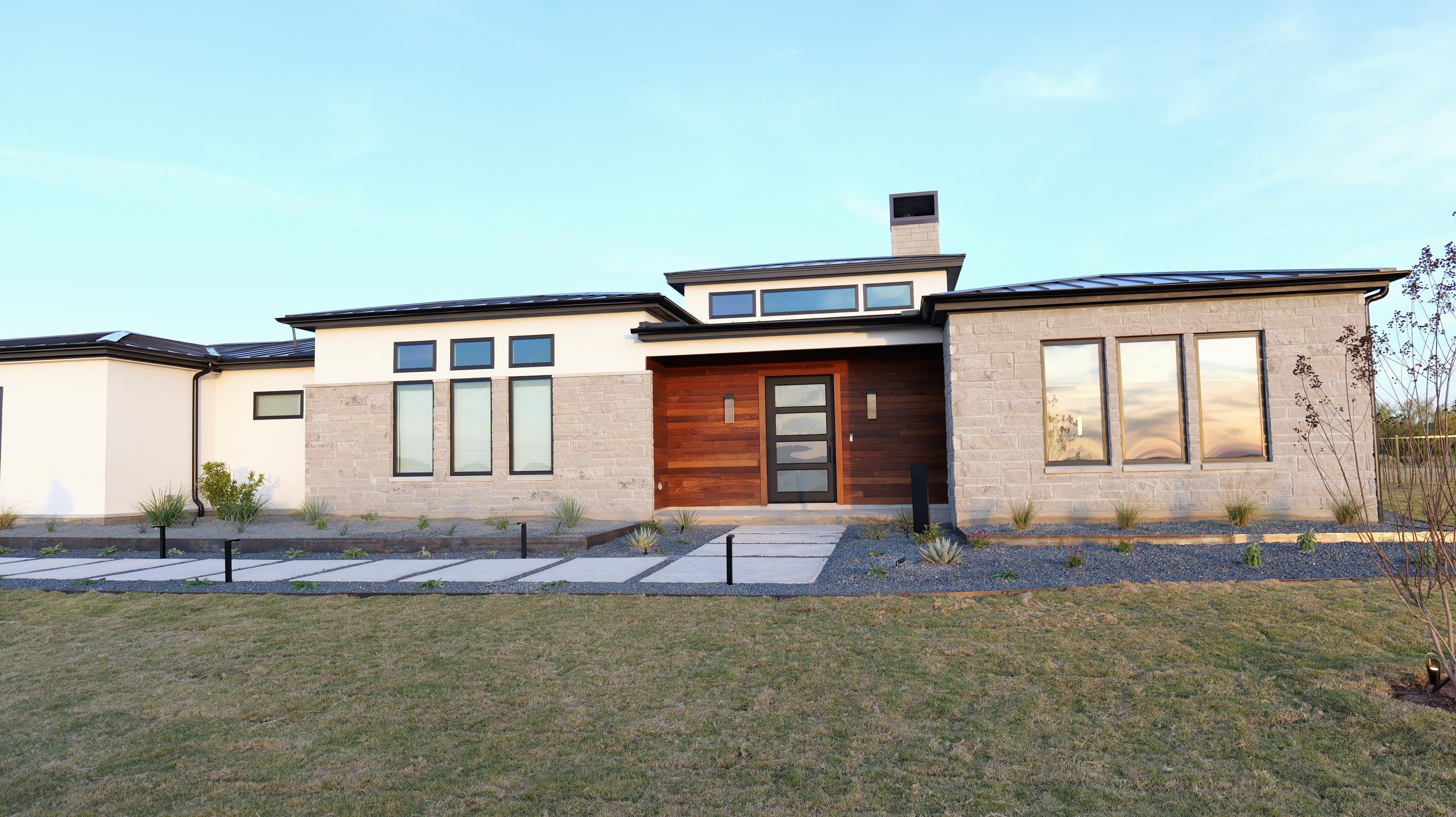 Front of a modern home at golden hour, a stained-wood entry between cut limestone and white stucco