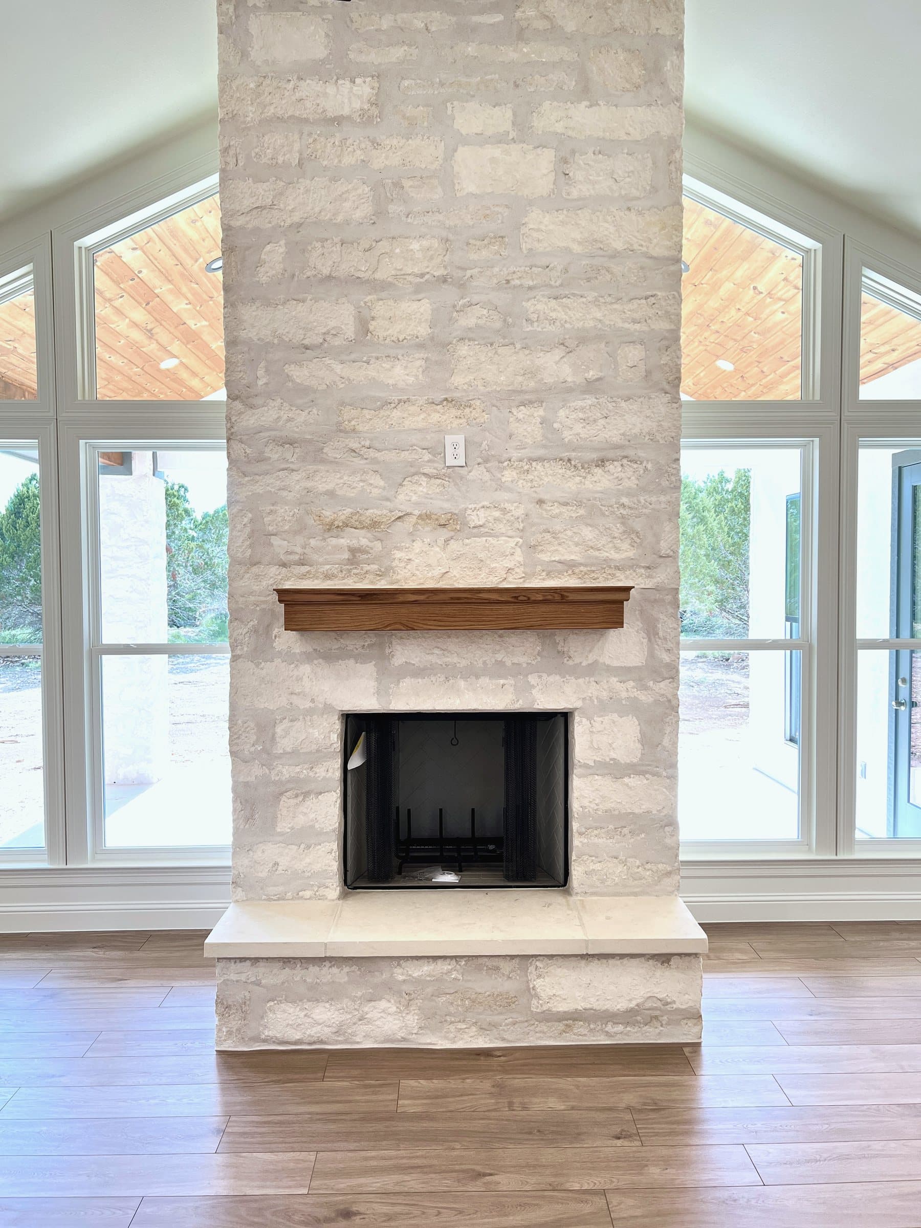 Floor-to-ceiling chopped-limestone fireplace with a cedar mantel between gabled windows
