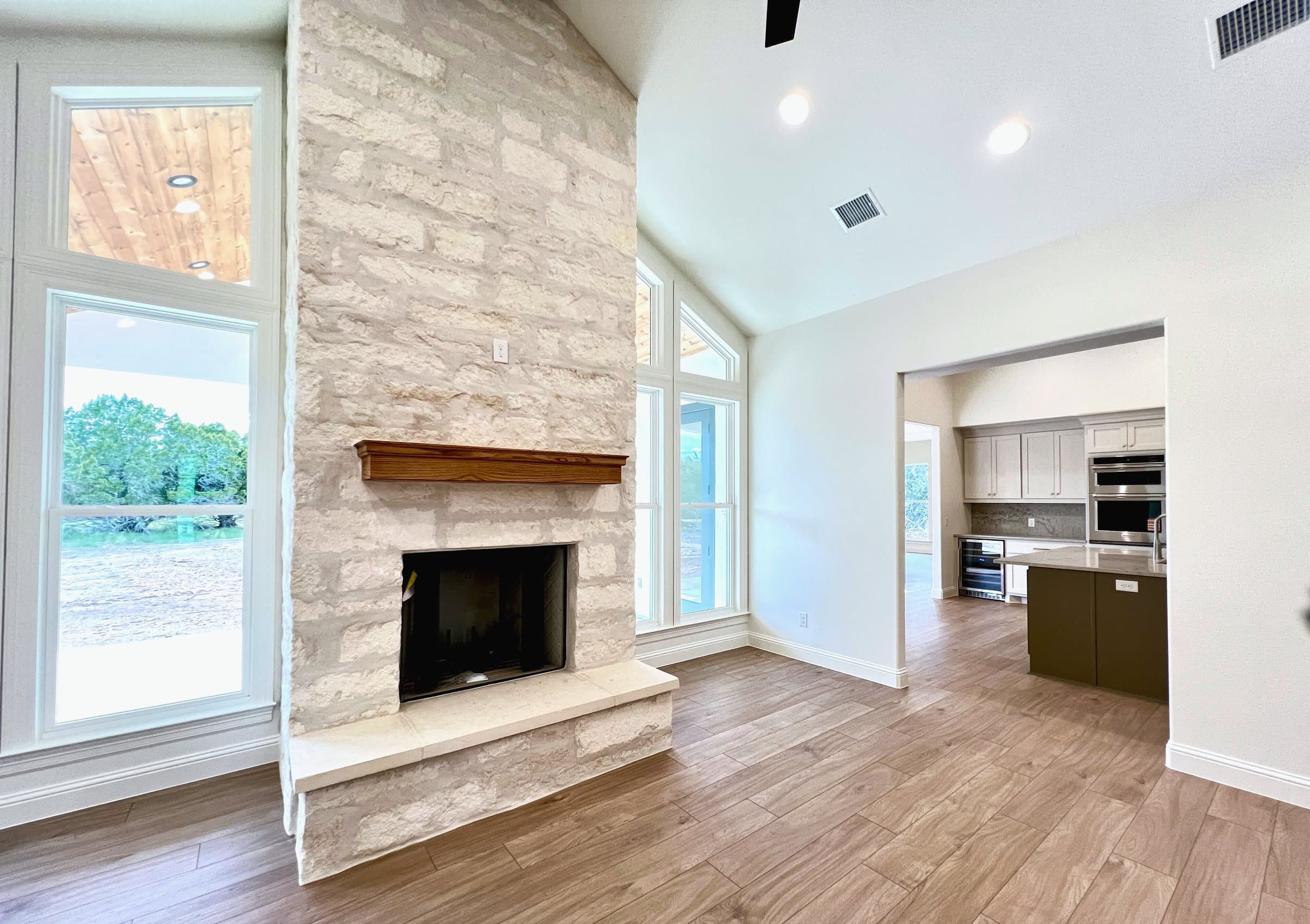 Living room with a limestone fireplace and clerestory windows, the kitchen beyond