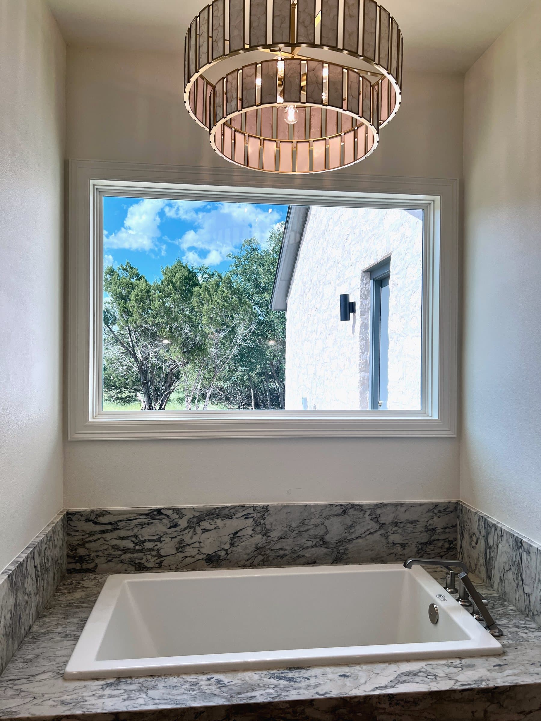 Primary bath tub beneath a drum chandelier, wrapped in veined marble